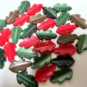 May include: A collection of leaf-shaped beads in various colors, including red, green, and brown. The beads are arranged in a scattered pattern, with a glossy finish. These decorative beads are suitable for jewelry making and craft projects.