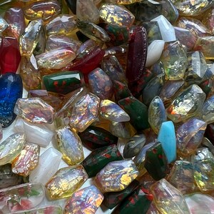 May include: A collection of polished gemstones in various colors, including red, blue, green, and clear. The stones have an iridescent quality, with flashes of gold and other colors. The gemstones are irregularly shaped and appear to be tumbled.