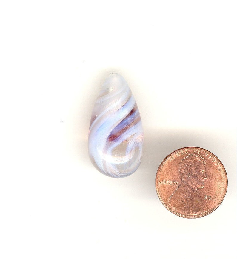 May include: A teardrop-shaped glass bead with swirling patterns of white, light blue, and maroon. A penny is next to the bead for size comparison. The bead is translucent and appears to be handmade, with a smooth, polished finish. The bead is likely for jewelry making.