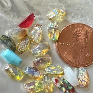 May include: A collection of various gemstone beads in shades of yellow, green, red, and blue. The beads are faceted and have an iridescent quality. A US penny is included for size reference.