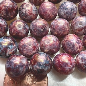 May include: A collection of round beads with a marbled appearance. The beads are primarily burgundy with swirls of blue and white. Each bead has a hole running through the center. A penny is included for size reference.