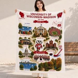 May include: A white fleece blanket featuring a map of the University of Wisconsin-Madison campus. It displays illustrations of Bascom Hall, Camp Randall Stadium, the Kohl Center, the State Capitol, and Lake Mendota, with a badger mascot in the center.
