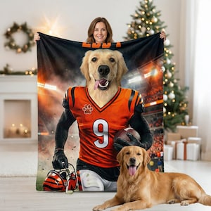 May include: A personalized blanket featuring a golden retriever in a football uniform with the number 9. The blanket has a black and orange color scheme, with the dog's face and body digitally superimposed. A second golden retriever is lying on the floor.