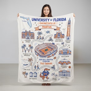 May include: A white University of Florida Gainesville map blanket featuring illustrations of campus landmarks, including Ben Hill Griffin Stadium, the Swamp, and the Century Tower. The blanket has a blue and orange color scheme and includes the name "Martha".