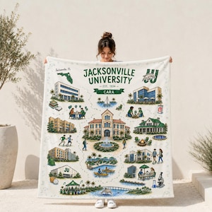 May include: A white fleece blanket featuring a detailed illustration of the Jacksonville University campus. The design includes various buildings, a fountain, palm trees, students, a dolphin mascot, and the text Jacksonville University Est. 1934.