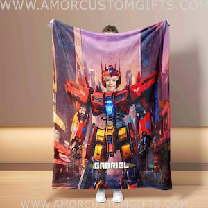 Puede incluir: Una manta personalizada con una vibrante ilustración de un personaje robot en tonos rojos, amarillos y azules, sobre un fondo de paisaje urbano. El nombre "GABRIEL" se muestra en texto blanco. Un artículo de decoración del hogar acogedor.