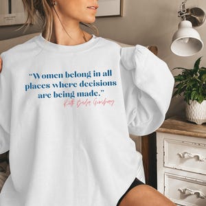 May include: White sweatshirt with a blue quote that reads "Women belong in all places where decisions are being made."  The quote is attributed to Ruth Bader Ginsburg.