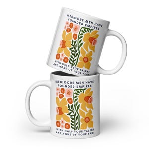Op de afbeelding: Twee witte keramische mokken gestapeld, elk met een bloemenontwerp van gele en oranje bloemen, groene bladeren en de tekst "MEDIOCRE MEN HAVE FOUNDED EMPIRES WITH HALF YOUR TALENT AND NONE OF YOUR RAGE."