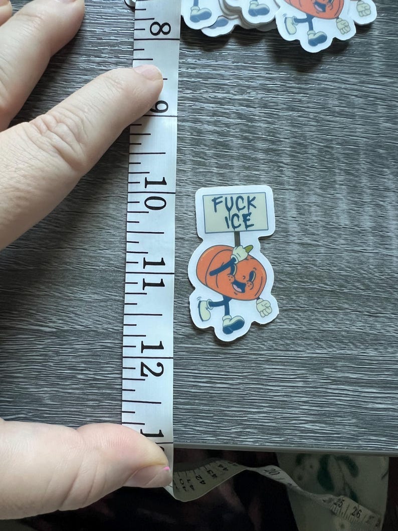 May include: A sticker featuring a cartoon pumpkin character holding a sign that reads "FUCK ICE." The pumpkin is orange with a smiling face, wearing blue shoes and gloves. The sticker measures approximately 2.5 inches in height.