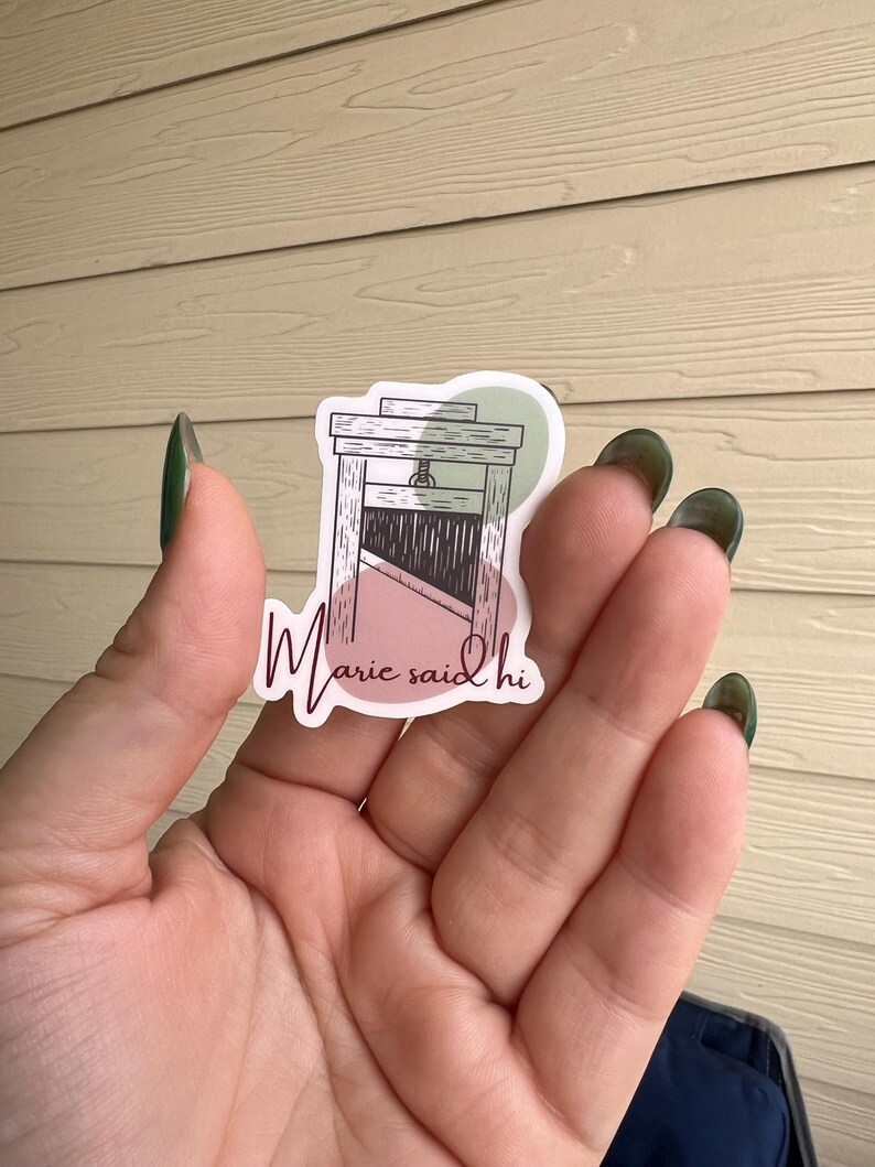 May include: A sticker with a pink and green background featuring a black and white illustration of a guillotine with the text "Marie said hi" in pink.