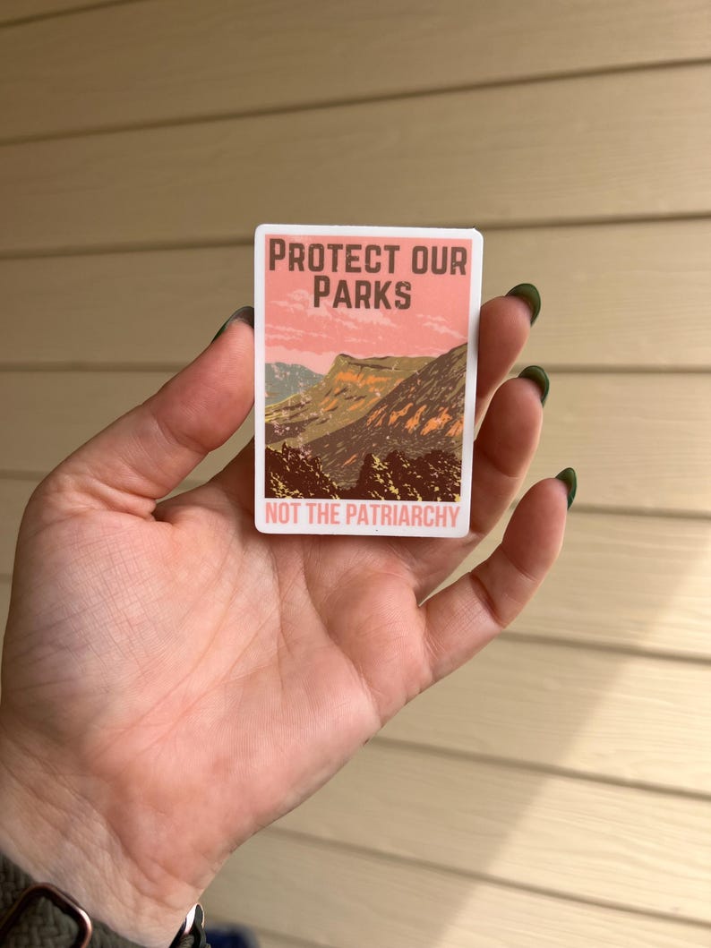 May include: A pink and white sticker with the text "Protect Our Parks Not The Patriarchy" and a mountain landscape image.