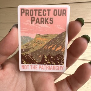 May include: A sticker with a vintage-style design featuring a mountain landscape and the text "Protect Our Parks Not The Patriarchy".