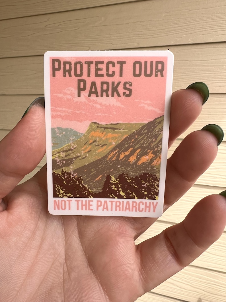 May include: A sticker with a vintage-style design featuring a mountain landscape and the text "Protect Our Parks Not The Patriarchy".