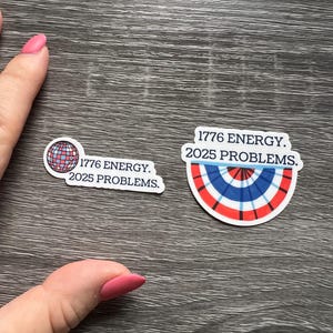May include: Two stickers with the text "1776 ENERGY. 2025 PROBLEMS." One sticker features a globe design with red, white, and blue sections. The other sticker has a red, white, and blue fan design.