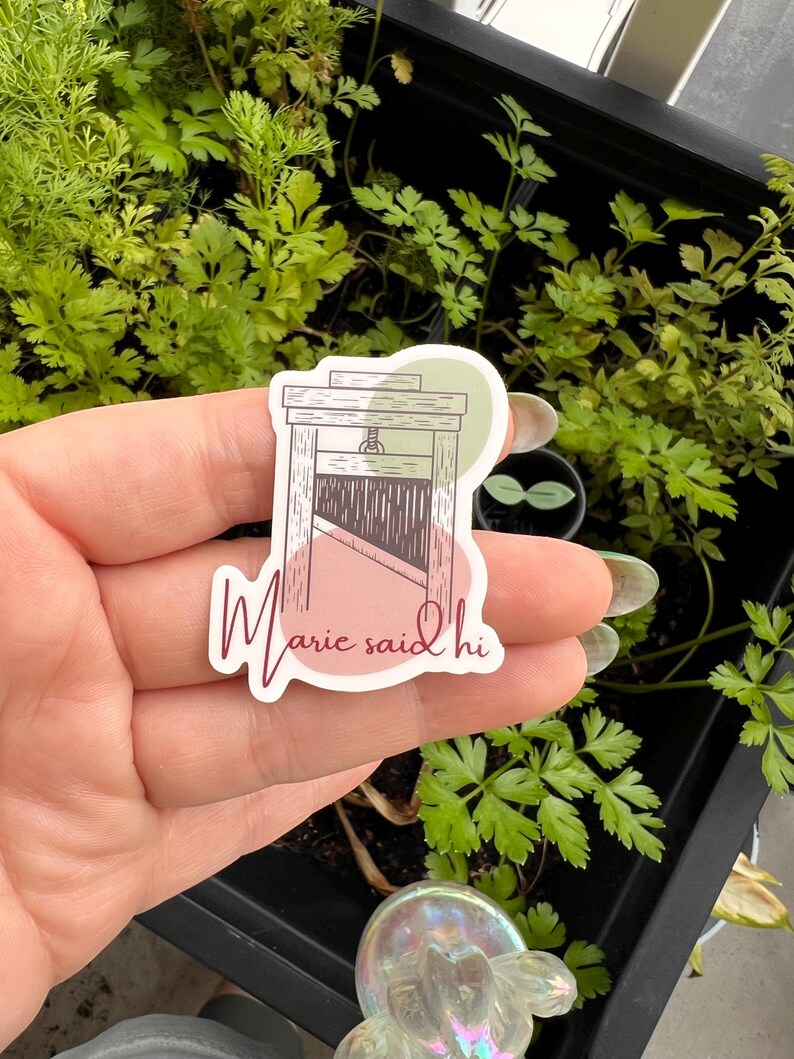 May include: A sticker with a drawing of a guillotine and the text "Marie said hi" in pink cursive lettering.