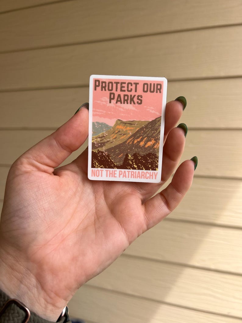 May include: A pink and brown sticker with the text "Protect Our Parks Not The Patriarchy" and a mountain scene.