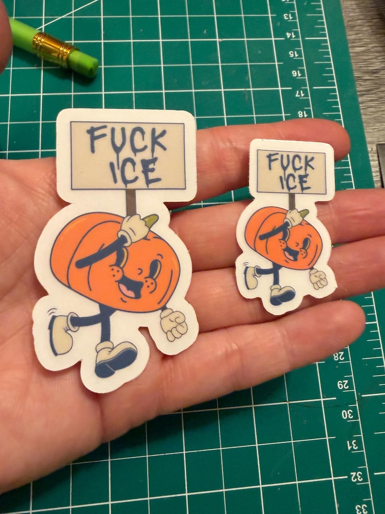 May include: Two die-cut vinyl stickers featuring a cartoon orange pumpkin character with a smiling face, wearing white gloves and blue shoes, holding a rectangular sign that reads FUCK ICE in dark blue lettering against a light background.