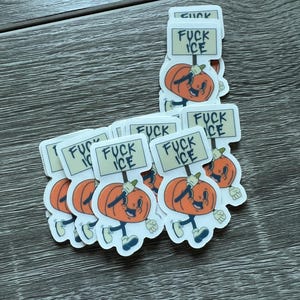 May include: A collection of stickers featuring a cartoon pumpkin character holding a sign that reads "FUCK ICE." The pumpkin is orange with a smiling face, blue shoes, and white gloves. The stickers are on a wooden surface.
