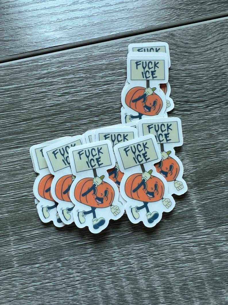 May include: A collection of stickers featuring a cartoon pumpkin character holding a sign that reads "FUCK ICE." The pumpkin is orange with a smiling face, blue shoes, and white gloves. The stickers are on a wooden surface.
