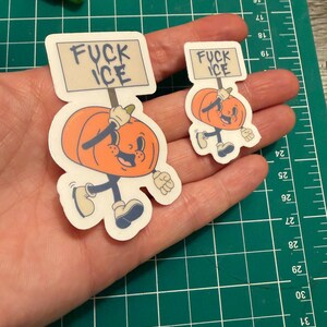 May include: Two die-cut stickers featuring an orange cartoon pumpkin character with a smiling face, arms, and legs. The pumpkin holds a rectangular sign above its head with the text FUCK ICE written in black capital letters on a light background.