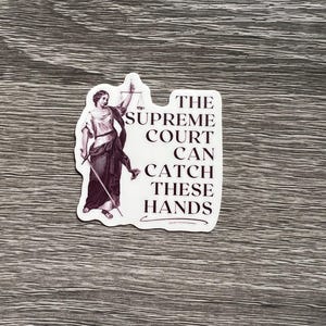 Op de afbeelding: Een witte sticker met een zwart-witte illustratie van een vrouw die een weegschaal en een zwaard vasthoudt. De tekst op de sticker luidt "The Supreme Court Can Catch These Hands".