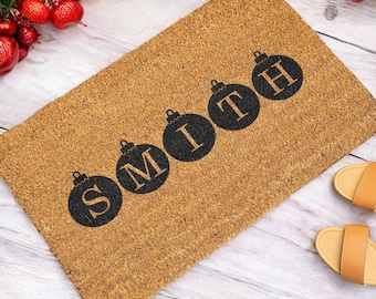 May include: A brown coir doormat with the word "SMITH" spelled out in black letters inside of black Christmas ornament shapes.