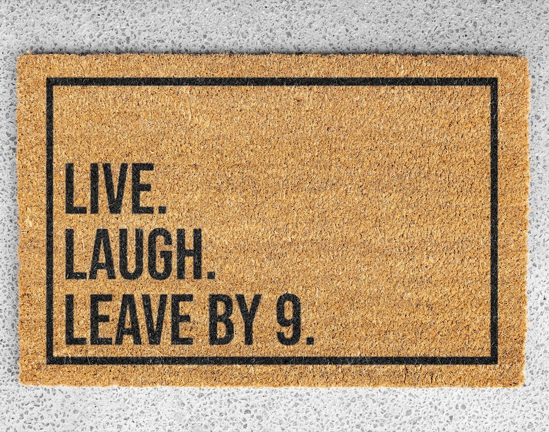 Op de afbeelding: Een bruine deurmat met zwarte tekst die "Live. Laugh. Leave by 9." luidt.