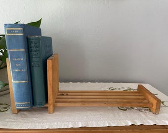 May include: A wooden book holder with three books. The books are blue and green with gold lettering. The book holder is made of light-colored wood and has a slatted design. The books are titled "Eleanor and Franklin" and "Peter and the Wolf".