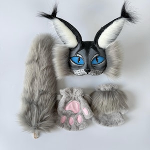May include: A gray and black faux fur animal mask with large pointed ears, bright blue eyes, and whiskers. The set includes a long, fluffy gray tail and two gray fingerless gloves featuring pink paw pads on the palms and furry cuffs.