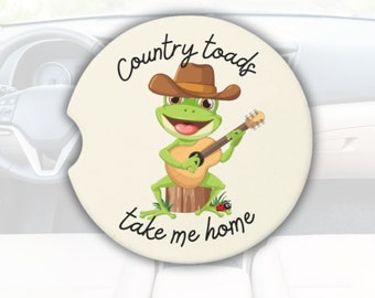 May include: A white round car coaster with a cartoon frog wearing a cowboy hat and playing a guitar. The text "Country toads take me home" is written around the frog.