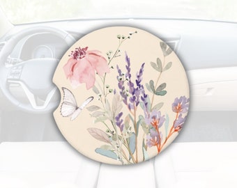 Könnte beinhalten: Ein runder Auto-Untersetzer mit einem Blumenmuster. Der Untersetzer zeigt eine rosa Blume, lila Blumen, grüne Blätter und einen weißen Schmetterling. Der Hintergrund ist hellbeige.