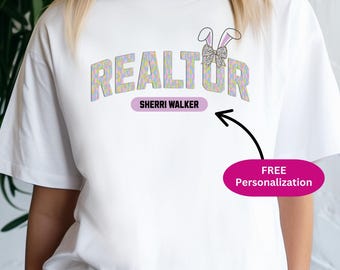 May include: A white t-shirt featuring the word REALTOR in a pastel-colored, patterned font. Above the letter O, there is a graphic of bunny ears with a leopard-print bow. Below the word, a purple bar contains the text SHERRI WALKER.