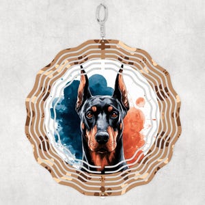 May include: A metal wind chime featuring a watercolor-style illustration of a Doberman Pinscher dog's head. The wind chime has a circular shape with multiple layers of metal, creating a swirling effect. The background is a mix of blue, orange, and white watercolor washes.