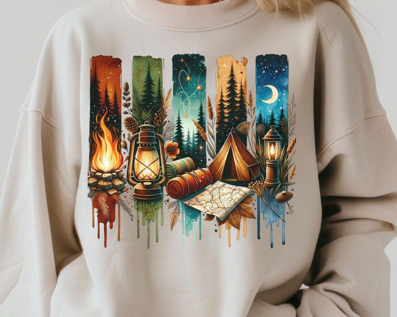 May include: A beige sweatshirt with a colorful graphic print of a campsite scene. The print features a campfire, a lantern, a tent, and a map. The colors in the print are red, orange, yellow, green, blue, and purple.