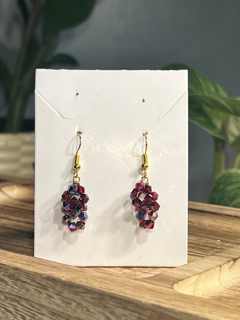 Peut inclure: Une paire de boucles d'oreilles pendantes avec un crochet dor&eacute; et un groupe de perles de cristal rouge.