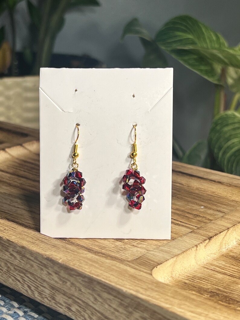 Peut inclure: Une paire de boucles d'oreilles pendantes avec des crochets dor&eacute;s et des perles de cristal rouges.