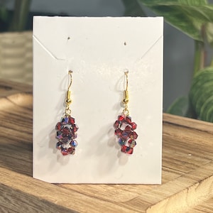 Peut inclure: Une paire de boucles d'oreilles pendantes avec un crochet dor&eacute; et des perles de cristal rouges.