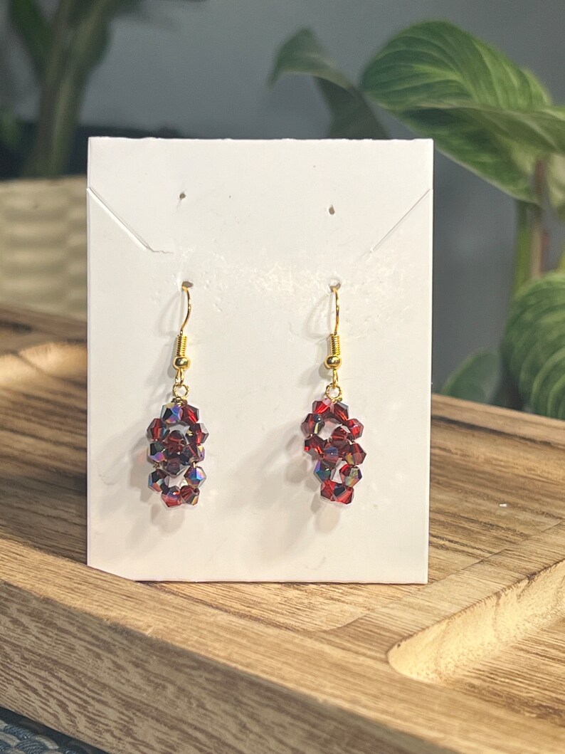 Peut inclure: Une paire de boucles d'oreilles pendantes avec un crochet dor&eacute; et des perles de cristal rouges.