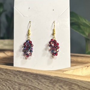 Peut inclure: Une paire de boucles d'oreilles pendantes avec des crochets dor&eacute;s et des perles de cristal rouges.