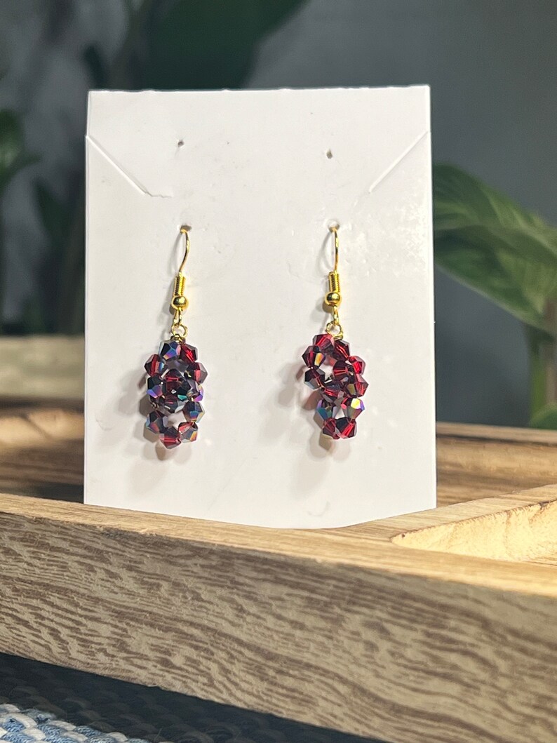 Peut inclure: Une paire de boucles d'oreilles pendantes avec des crochets dor&eacute;s et des perles de cristal rouges.
