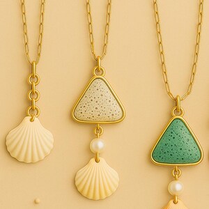 May include: Gold-toned necklaces with seashell pendants. Each necklace features a different pendant design: a seashell, a triangle with a speckled surface, and a triangle with a green speckled surface. Each pendant is paired with a seashell and a pearl.