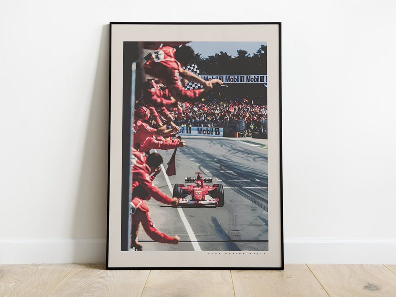 K&ouml;nnte beinhalten: Ein roter Formel-1-Rennwagen rast &uuml;ber die Ziellinie, im Hintergrund jubelt eine Menschenmenge in roten Overalls. Das Auto ist ein Ferrari mit der Nummer 1 an der Seite. Die Worte "Mobil 1" sind auf der Strecke zu sehen.