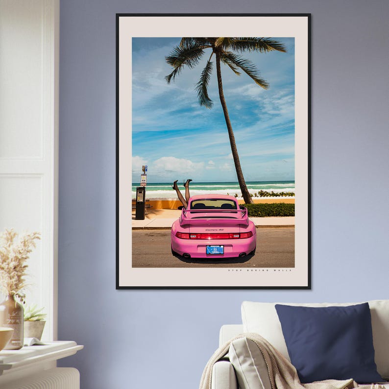 Puede incluir: Un Porsche 911 rosa convertible estacionado en una playa con una palmera de fondo. El coche est&aacute; de frente a la c&aacute;mara y el techo est&aacute; bajado. Dos piernas sobresalen de la parte trasera del coche.