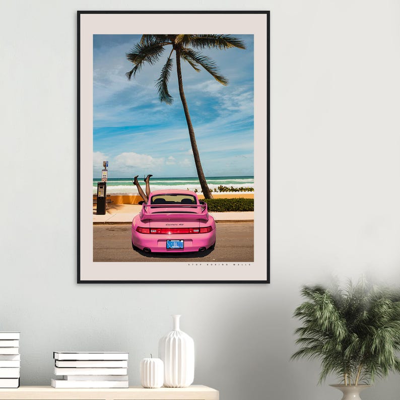 Puede incluir: Un Porsche 911 rosa estacionado en una calle con una palmera de fondo. Las piernas de una persona sobresalen de la parte trasera del coche.