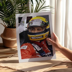 May include: A close-up of a race car driver wearing a yellow and black helmet with the word "Marlboro" on it. The driver is wearing a red racing suit with the words "Nacional" and "Boss" on it. The driver is winking at the camera.