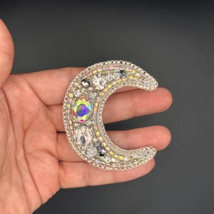 May include: A silver crescent moon brooch with iridescent and clear rhinestones.
