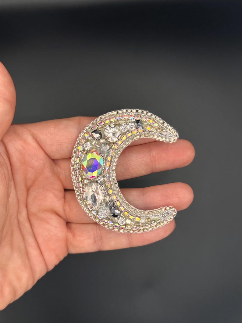 May include: A silver crescent moon brooch with iridescent and clear rhinestones.
