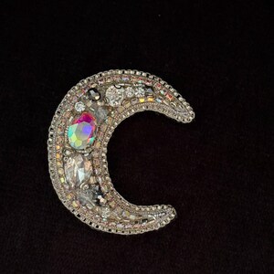 May include: A silver crescent moon brooch with iridescent and clear rhinestones.