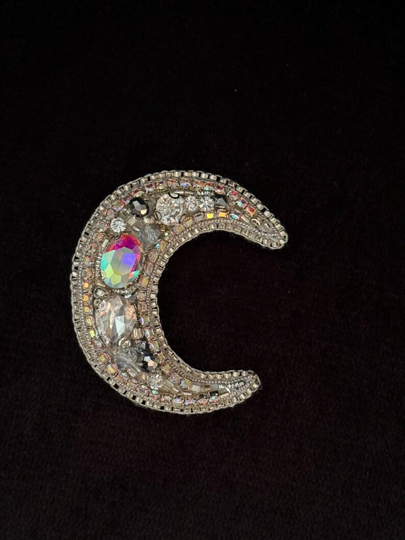 May include: A silver crescent moon brooch with iridescent and clear rhinestones.