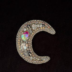 May include: A silver crescent moon brooch with iridescent and clear rhinestones.
